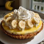 A beautiful, finished banana cream pie topped with sliced bananas, yellow custard, and a large swirl of whipped cream.