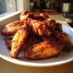 A close-up of a pile of perfectly cooked, crispy, and glazed chicken wings on a white plate.