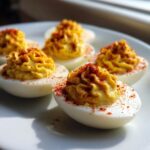 Close-up of several perfectly piped deviled eggs sprinkled generously with bright red paprika.