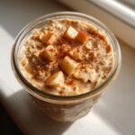 Overhead view of apple cinnamon overnight oats topped with diced apples and cinnamon in a glass jar.