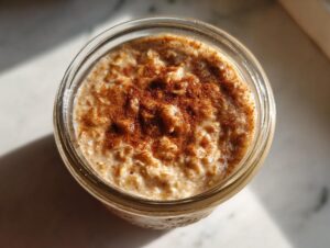Overhead view of creamy apple cinnamon overnight oats topped generously with ground cinnamon in a glass jar.