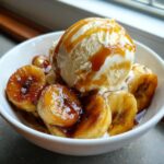 Close-up of caramelized bananas foster topped with a scoop of vanilla ice cream and caramel drizzle.