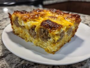 A golden-brown square slice of breakfast casserole with sausage and cheese, served on a white plate.