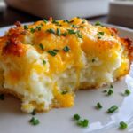 A close-up of a serving of baked mashed potatoes topped with melted cheddar cheese and fresh chives.