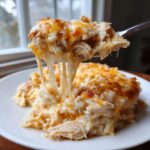 A fork lifts a portion of cheesy chicken and rice, showing long, gooey cheese pulls.