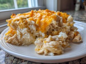 A generous serving of cheesy chicken and rice casserole topped with melted cheddar cheese on a white plate.