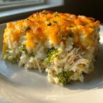 A close-up slice of creamy chicken and broccoli rice casserole topped with melted cheddar cheese.