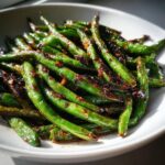 A close-up of vibrant green beans coated in a dark, savory garlic sauce, ready to serve.