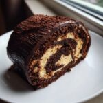 Close-up of a slice of chocolate Bûche de Noël cake showing the dark sponge and light cream swirl filling.