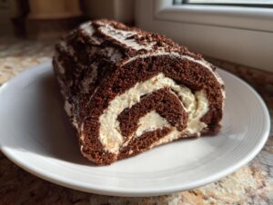 A cross-section slice of chocolate Bûche de Noël cake rolled with white cream filling, dusted with powdered sugar.