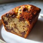 A close-up of a moist slice of chocolate chip banana bread showing melted chocolate chunks and a golden-brown top.