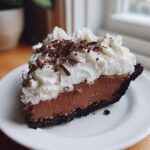 A decadent slice of Christmas chocolate cream pie featuring a dark crust, rich chocolate filling, and tall whipped cream topping with chocolate shavings.