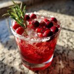A vibrant red cranberry pomegranate margarita garnished with fresh cranberries, pomegranate seeds, and a sprig of rosemary.
