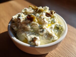 Close-up of a creamy, white dirty martini dip topped with blue cheese crumbles and sliced green olives.