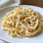 Close-up of fettuccine pasta coated in rich homemade alfredo sauce and topped with cracked black pepper.