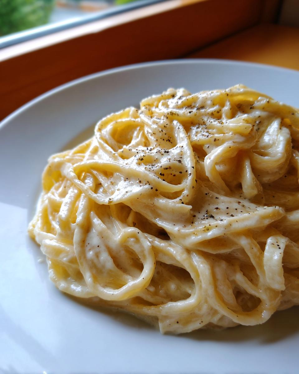 Close-up of fettuccine pasta coated in rich homemade alfredo sauce and topped with cracked black pepper.