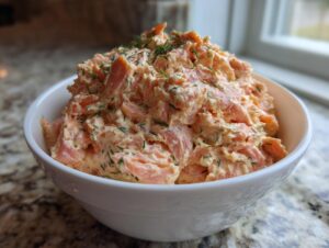 A generous serving of creamy salmon dip, mixed with dill, mounded in a white bowl.