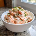 A white bowl filled with chunky, creamy salmon dip, garnished generously with fresh dill.
