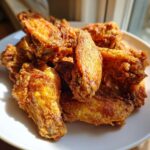 A close-up of a pile of golden brown, crispy baked chicken wings on a white plate.