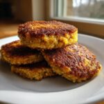 A stack of four golden brown, crispy fried cornbread patties resting on a white plate.
