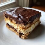 A square slice of layered eclair cake with graham crackers, vanilla cream, and thick chocolate frosting.