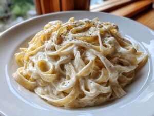 Close-up of fettuccine pasta coated heavily in creamy homemade alfredo sauce and topped with black pepper.