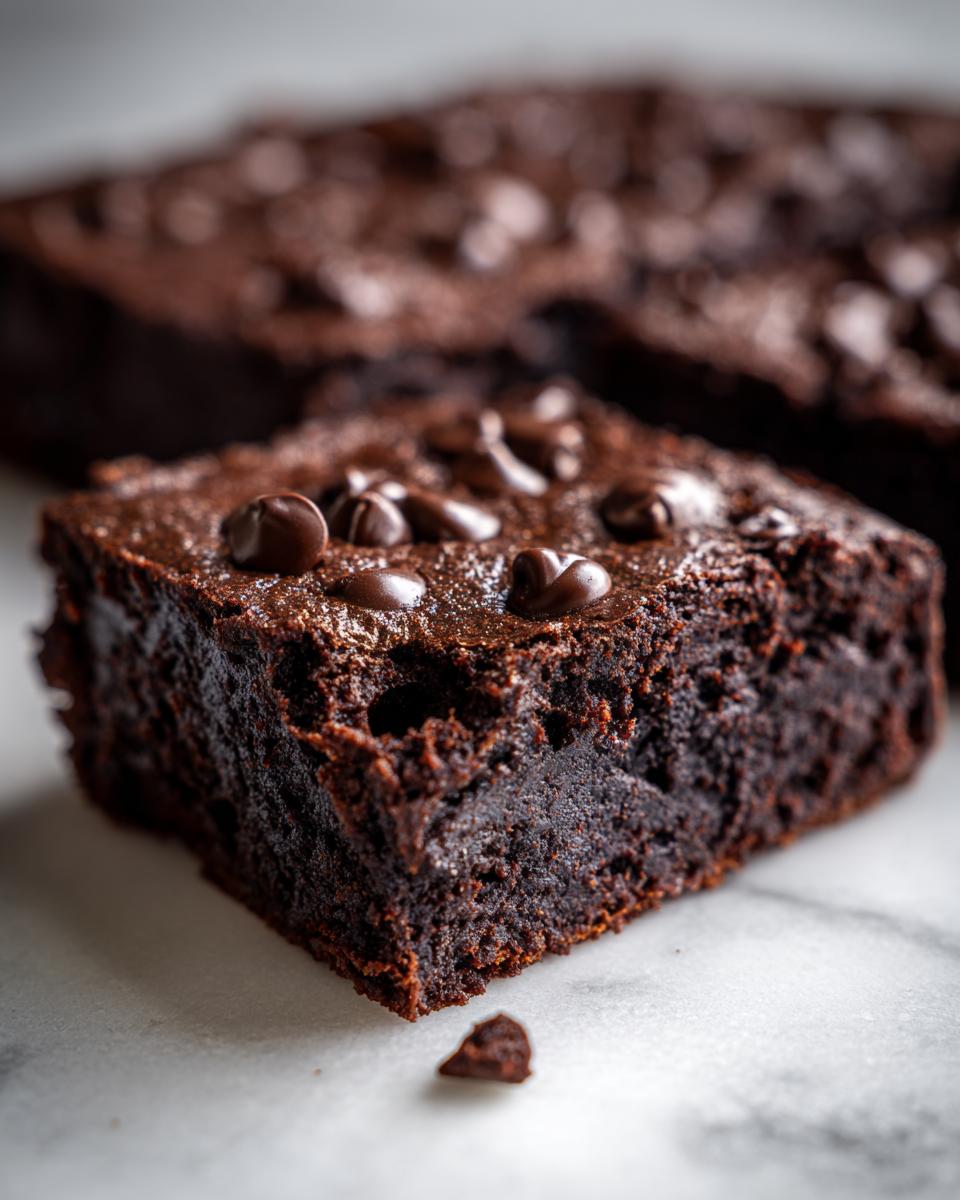 A rich, fudgy square of Sweet potato brownies topped with melted chocolate chips, resting on a marble surface.