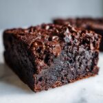Close-up of a rich, fudgy slice of sweet potato brownies topped with melted chocolate chips on a white marble surface.