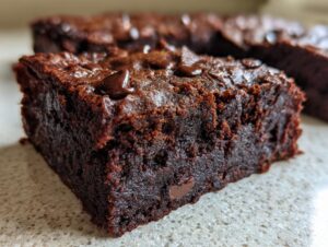 A close-up view of a thick, fudgy slice of sweet potato brownies topped with melted chocolate chips.