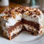 A slice removed from a decadent German Chocolate Pie showing layers of chocolate filling, cream, and pecan topping.