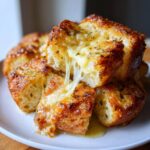 Close-up of golden brown cheese bread pieces stacked, showing a dramatic cheese pull from the melted cheese.