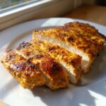 Close-up of perfectly cooked, sliced greek chicken breast with a golden, seasoned crust.