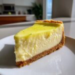 A close-up slice of creamy key lime cheesecake on a white plate, topped with lime zest.