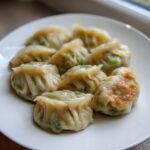 A close-up of several Traditional Chinese Dumplings, partially steamed and one pan-fried, served on a white plate.