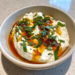 A close-up of whipped ricotta dip topped with a drizzle of hot honey and fresh chopped mint leaves.