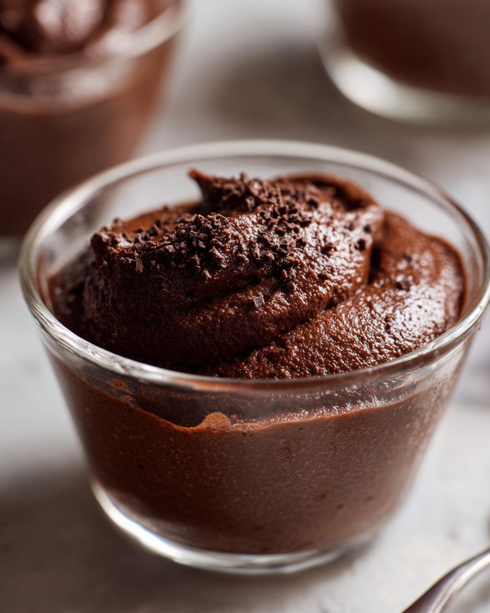 Close-up of rich, dark chocolate mousse topped with chocolate shavings in a small glass serving cup.