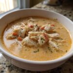 Close-up of a white bowl filled with rich, creamy crab soup loaded with chunks of white and red crab meat.