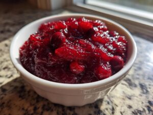 Close-up of homemade cranberry sauce, rich red and chunky, served in a small white bowl.