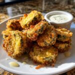 A plate piled high with crispy, golden brown Fried Pickles served with a small ramekin of creamy dipping sauce.