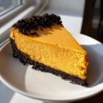 A perfect slice of amazing pumpkin cheesecake with a dark chocolate crust, sitting on a white plate.