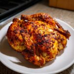 A whole, perfectly cooked spatchcock chicken with crispy, seasoned skin resting on a white plate.