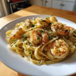 A close-up, appetizing photo of shrimp alfredo pasta tossed in creamy sauce, topped with sautéed shrimp and parsley.