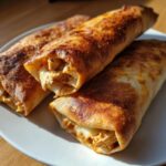 Three golden brown, crispy Baked Chicken Chimichangas piled on a white plate, showing shredded chicken filling.