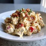 A serving of creamy BLT chicken salad mixed with diced tomatoes and topped with crispy bacon and chives.