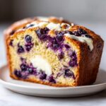 Close-up of a moist slice of Blueberry Cream Cheese Bread showing swirls of cream cheese and bursting blueberries.