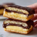 Two stacked boston cream pie cookies cut in half showing vanilla custard filling and chocolate ganache topping.