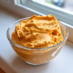 A clear glass bowl filled with thick, whipped orange pumpkin fluff dessert mixture.