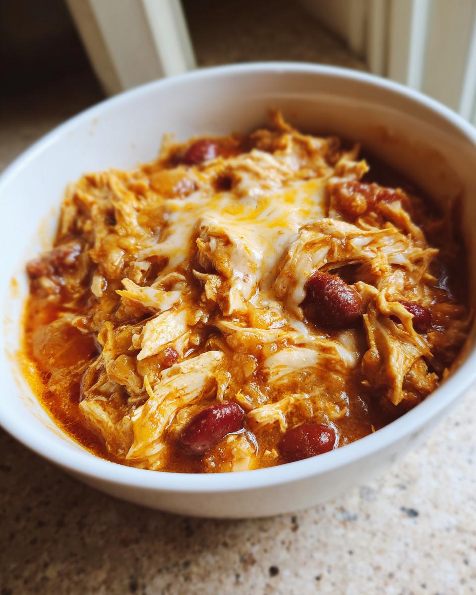 Close-up of a white bowl filled with rich, saucy buffalo chicken chili topped with melted white cheese.