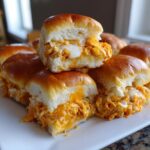 A stack of delicious buffalo chicken sliders featuring shredded orange buffalo chicken and melted white cheese inside soft rolls.