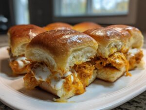 Close-up of several gooey buffalo chicken sliders with melted cheese and sauce on soft rolls.